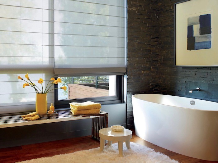 Btahroom with dark stone tile, oval tub and large windows with coverings.